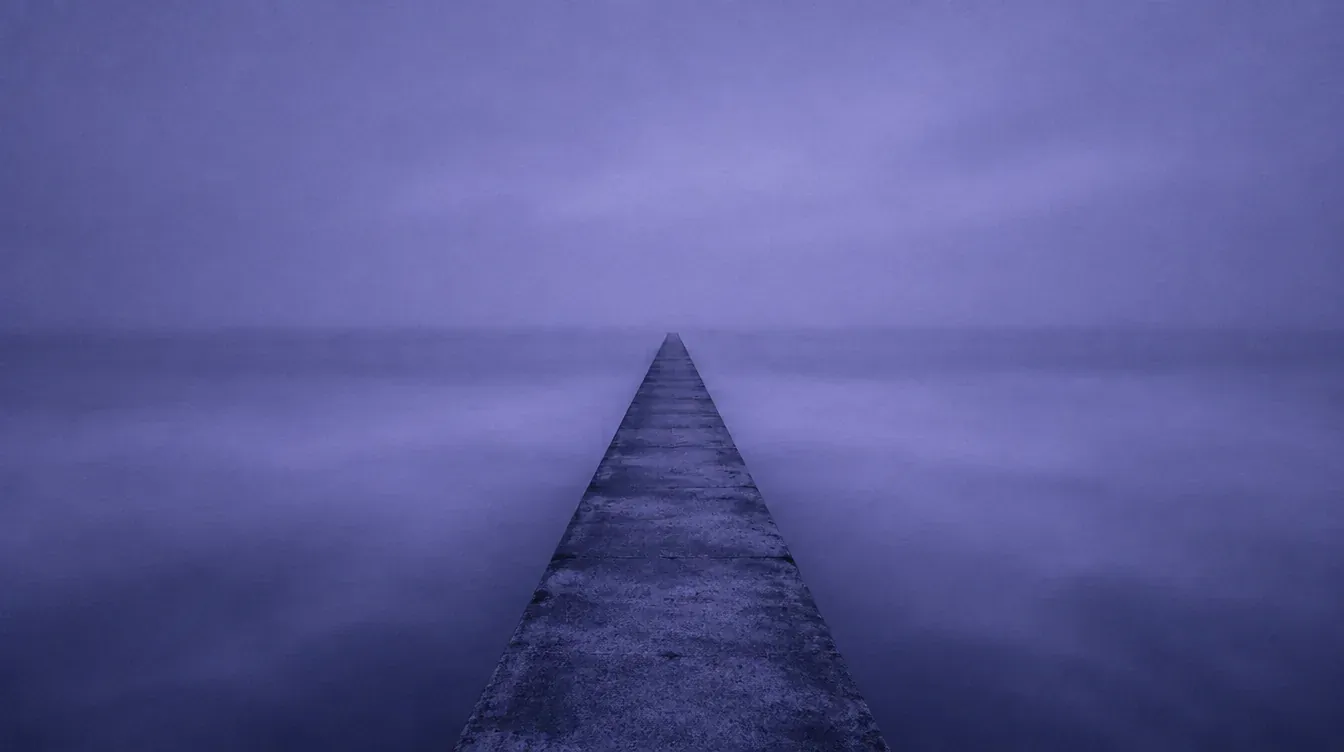 A long pier disappearing into a calm, misty sea
